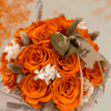 Jesienny flower box w kolorze dyni zbliżenie – welurowe pudełko z bukietem intensywnie pomarańczowych róż, białymi dodatkami i złotym serduszkiem z napisem „rękodzieło”.