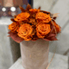 Jesienny flower box w kolorze dyni na podeście – welurowe pudełko z bukietem intensywnie pomarańczowych róż, białymi dodatkami i złotym serduszkiem z napisem „rękodzieło”.