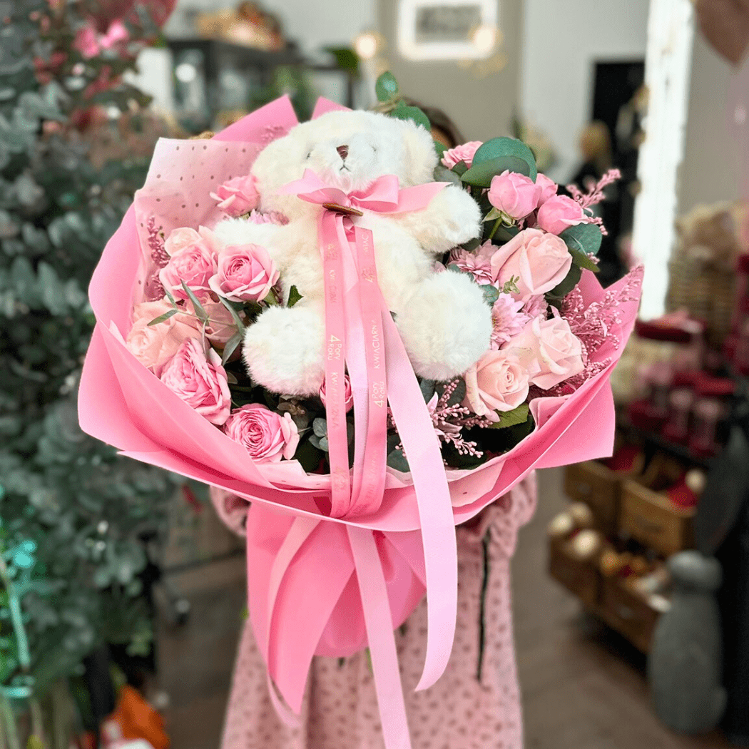 bukiet jasnych kwiatów, róż z pluszowym misiem w różowym papierze