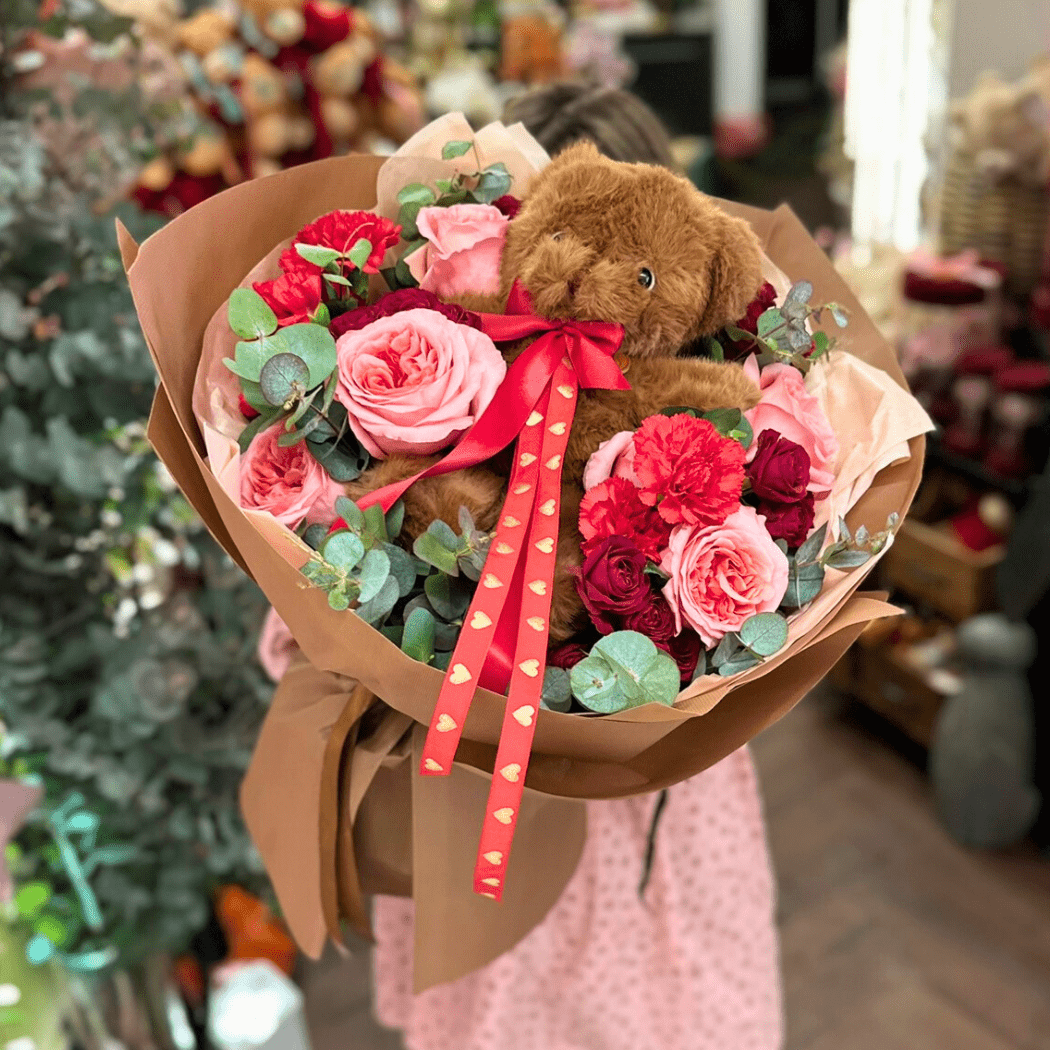 bukiet różowych i czerwonych kwiatów z eukaliptusem, na środku pluszowy miś