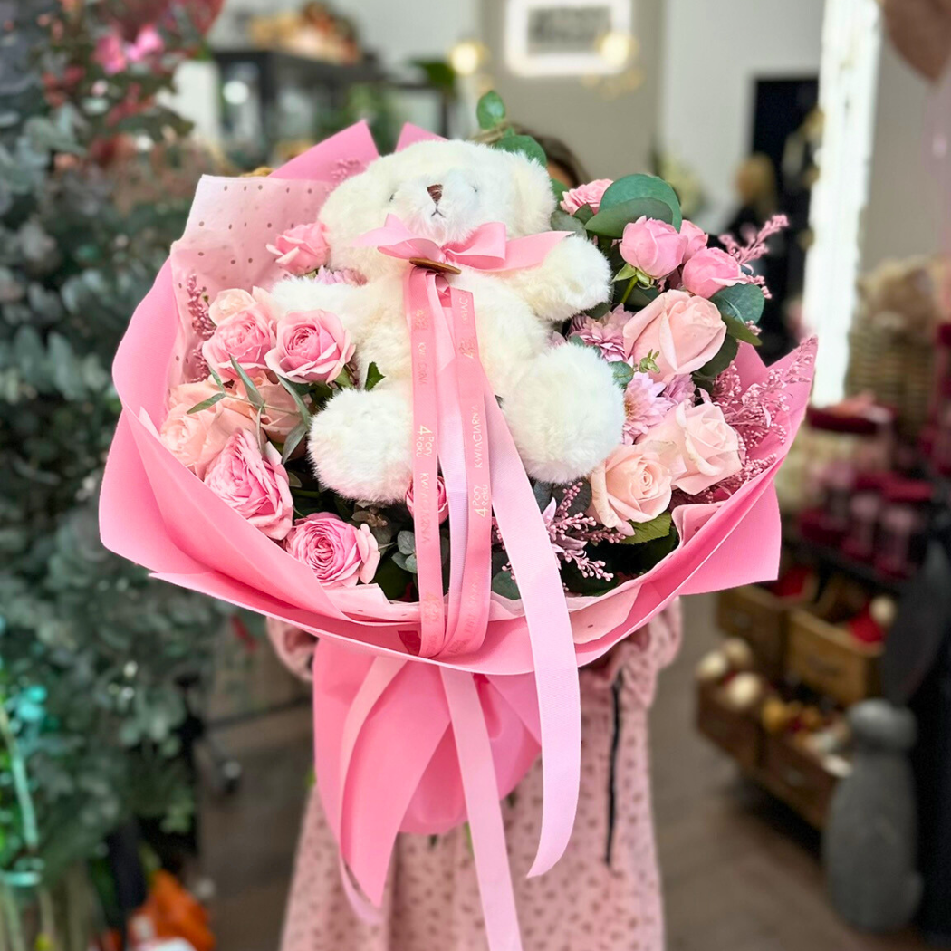 bukiet jasnych kwiatów, róż z pluszowym misiem w różowym papierze