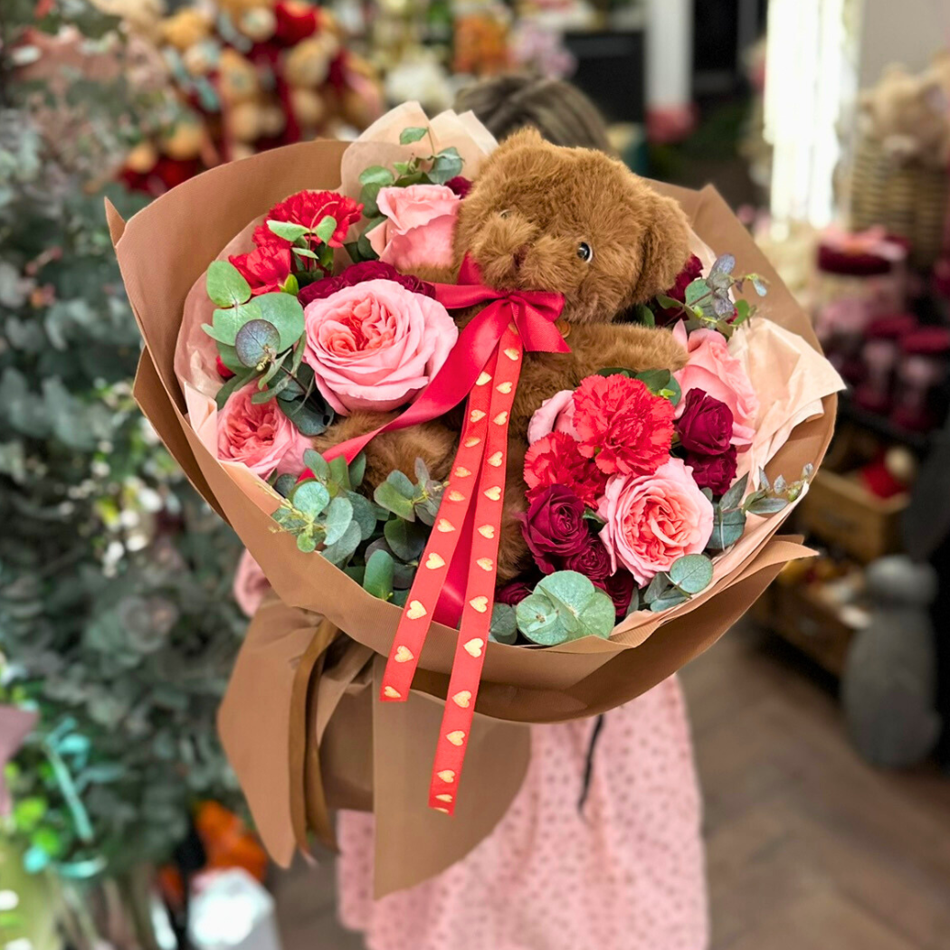 bukiet różowych i czerwonych kwiatów z eukaliptusem, na środku pluszowy miś